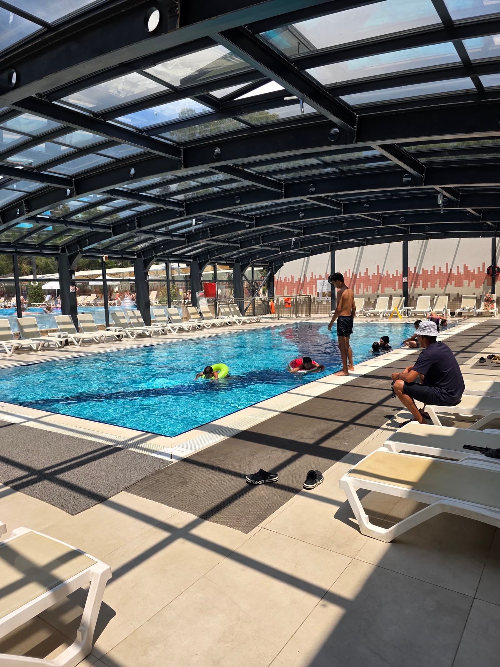 Piscina acoperită a hotelului, sub o cupolă de sticlă și metal, cu șezlonguri albe pe margine.