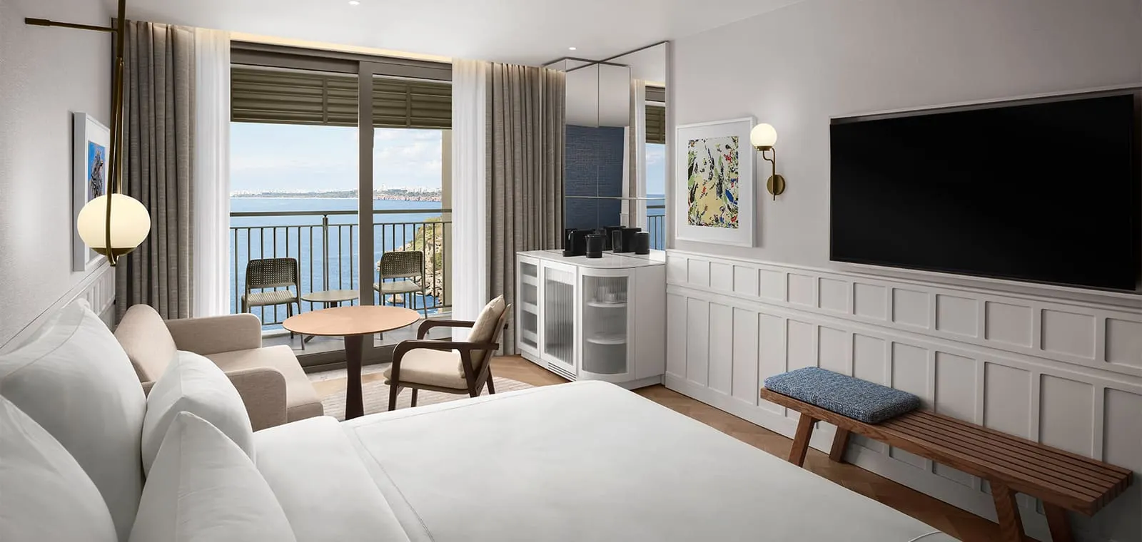 Cameră deluxe cu pat alb, perete în lambriuri, televizor și balcon cu vedere spre mare și spre oraș.